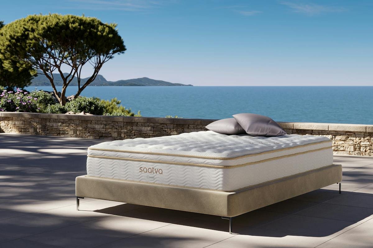 A Saatva Classic mattress on a dark upholstered bed frame between two nightstands with lamps