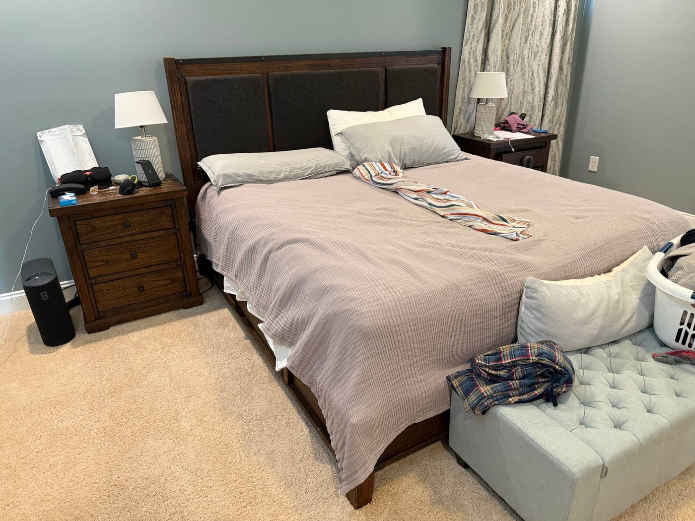 The author's bedroom: an unmade king bed with a gray quilt and pillows, wooden nightstands, and the black Eight Sleep Pod hub on the floor beside the left nightstand